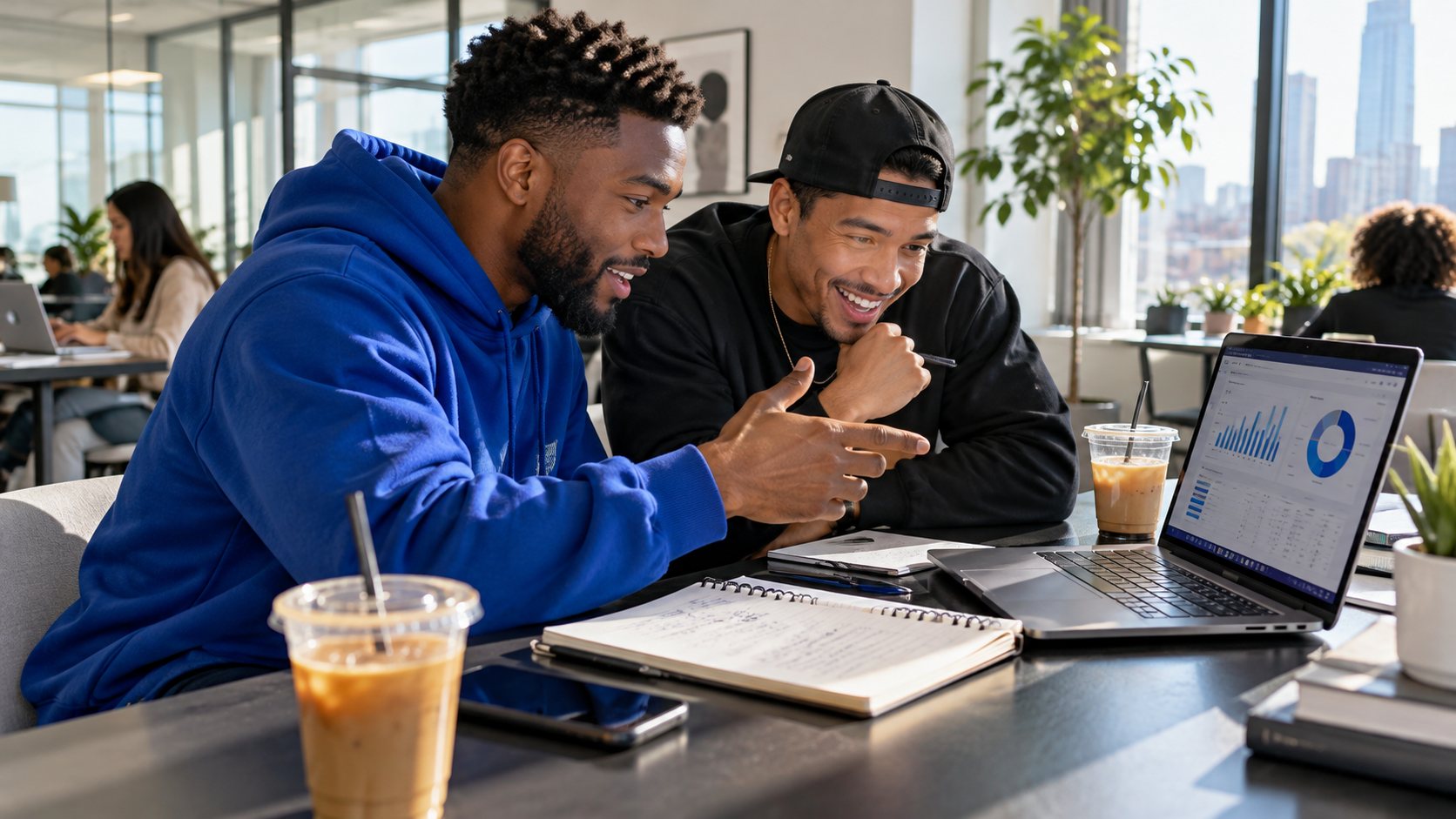 Two friends at a bright coworking space, excited as they plan their finances together with a laptop and a notebook